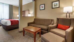 A hotel room with a bed, a sofa, a chair, a small table, and a lamp.