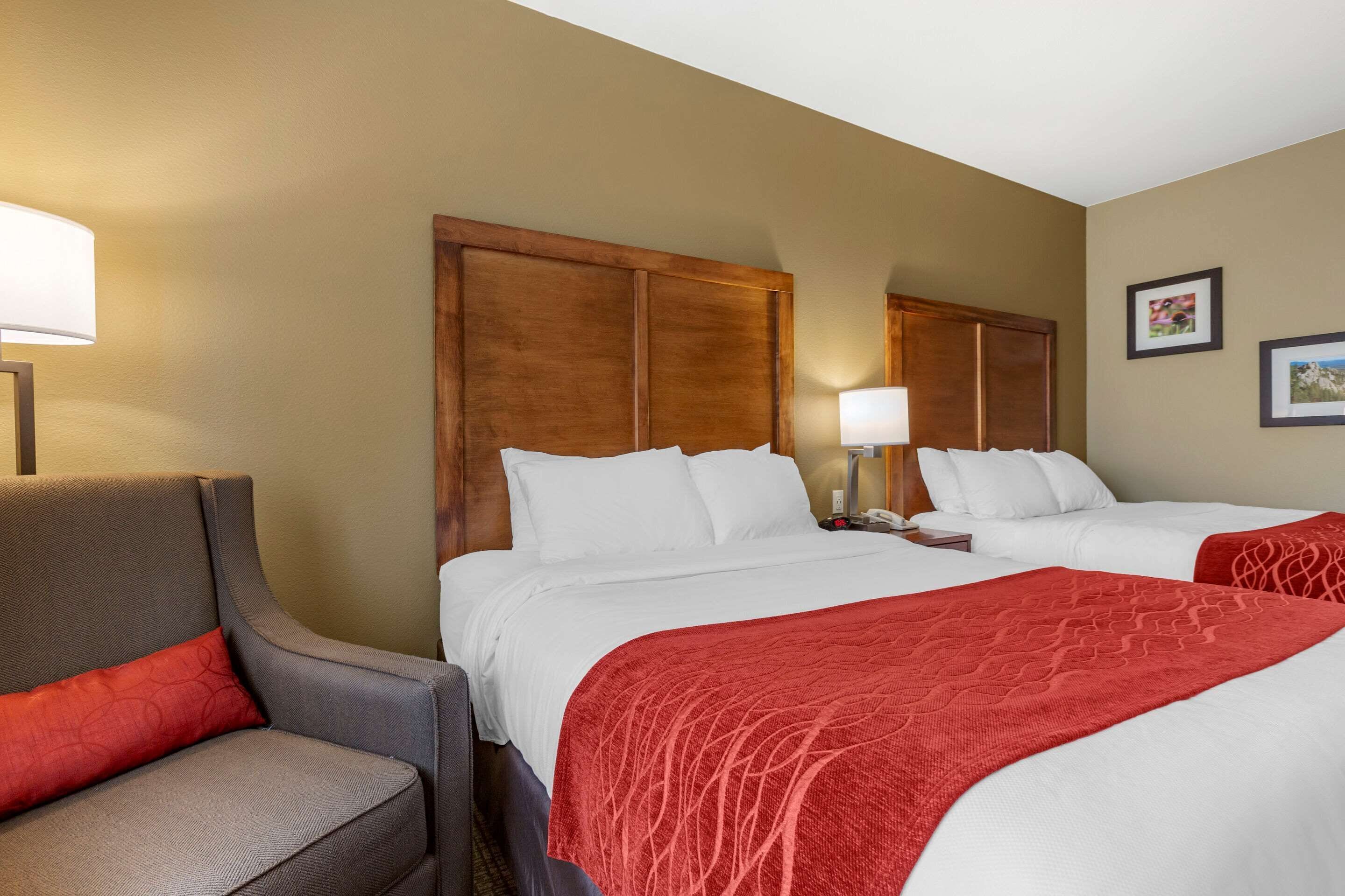 Una habitación de hotel con dos camas, un sillón gris y una manta roja.