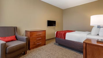 Quarto de hotel com cama, cadeira, cômoda e TV fixada na parede.