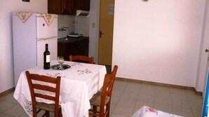 Un pequeño comedor con una mesa dispuesta para dos, una botella de vino y una copa. Se observa un mueble de madera sobre la mesa y una puerta a la derecha.