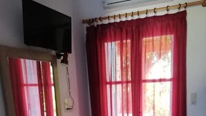 Una habitación con un aparador de madera, un televisor de pantalla plana montado en la pared y una ventana con cortinas rojas.