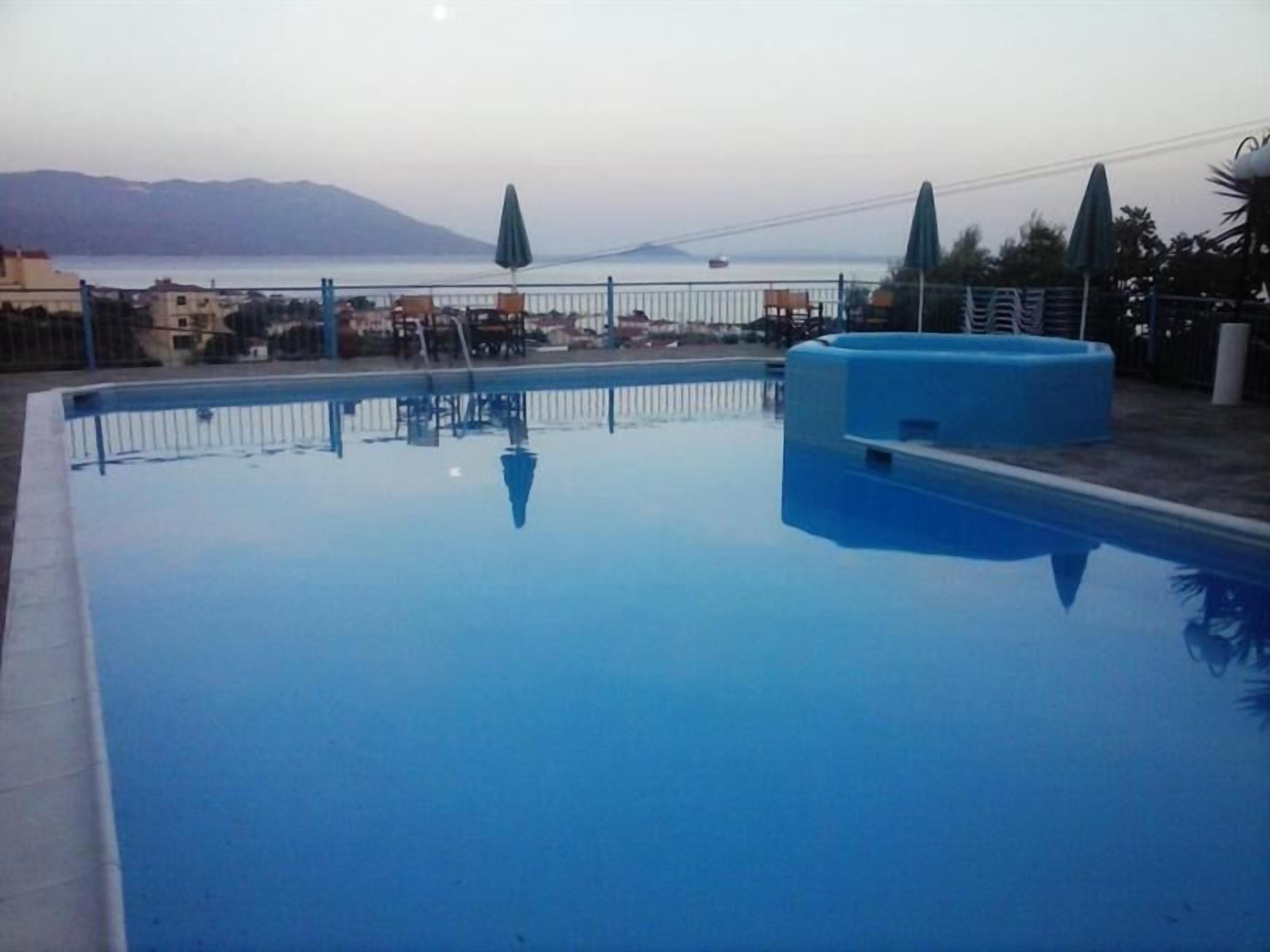 A rectangular swimming pool with a blue interior, surrounded by a white fence. In the background, there is a view of a bridge and distant mountains.