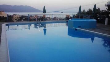 A rectangular swimming pool with a blue interior, surrounded by a white fence. In the background, there is a view of a bridge and distant mountains.