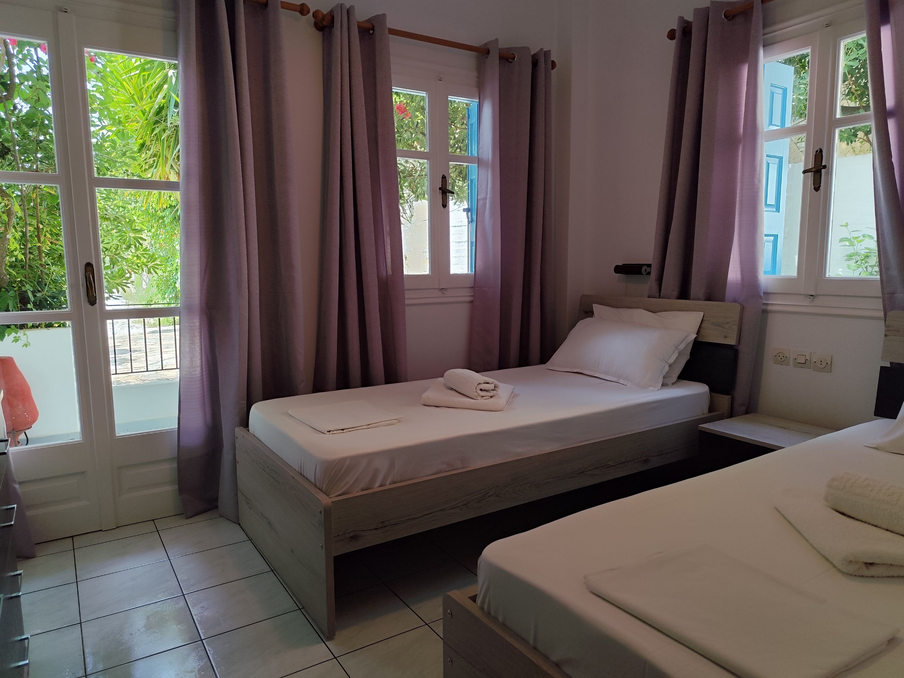 Un dormitorio con cama, mesita de noche, ventana con cortinas y vista a espacios verdes.