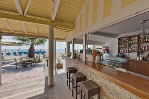 A beachside bar with outdoor seating, a stone counter, and a view of the beach and ocean. - Olympios Zeus (Dio-Olympos)