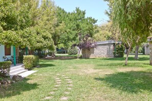 A courtyard with stone buildings, a paved path, and lush greenery. - Olympios Zeus (Dio-Olympos)