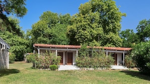 A two-story house with a red-tiled roof, a porch with a railing, and a stone wall on one side.