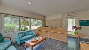 A modern reception area with a reception desk, seating area with a sofa and chairs, a coffee table, and large windows offering a view of greenery outside.