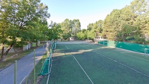 An outdoor tennis court surrounded by trees, with a fence and a net.