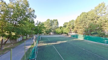 Ein Tennisplatz im Freien, umgeben von Bäumen, mit Zaun und Netz.