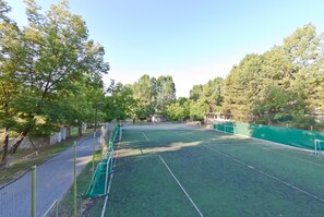 Ein Tennisplatz im Freien, umgeben von Bäumen, mit Zaun und Netz.