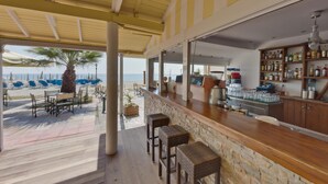 A beachside bar with outdoor seating, a stone counter, and a view of the beach and ocean. - Olympios Zeus (Dio-Olympos)