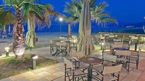 An outdoor dining area with tables and chairs, palm trees, and a view of the beach at night.