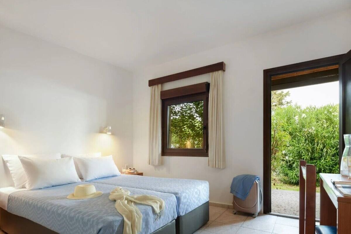 Habitación de hotel con cama, ventana con cortinas, escritorio con silla y vista a zonas verdes.
