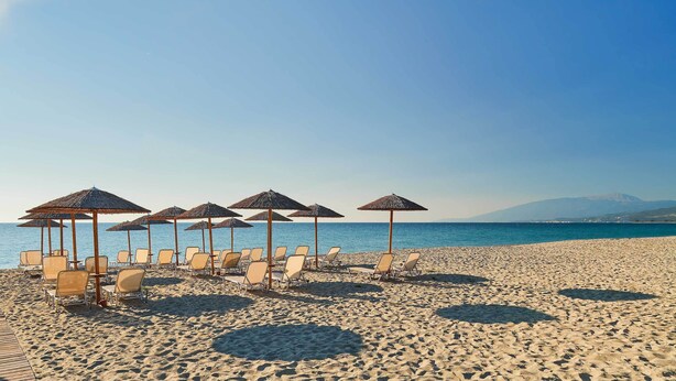 A beach with sun loungers and umbrellas, a wooden deck, and a view of the sea and mountains. - Olympios Zeus (Dio-Olympos)