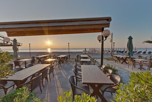 An outdoor seating area with tables and chairs, overlooking a body of water and a distant shoreline. - Olympios Zeus (Dio-Olympos)