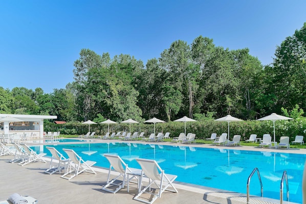 A swimming pool with lounge chairs and umbrellas, surrounded by trees.