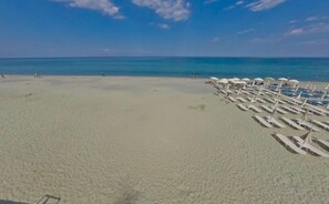 A beach with rows of sun loungers and umbrellas, a clear sky, and the ocean in the background. - Olympios Zeus (Dio-Olympos)