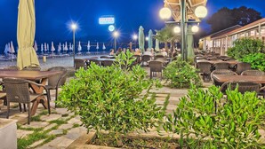 An outdoor seating area with tables and chairs, a sign for 'PIZZA SPAGHETTI', and a view of the beach at night. - Olympios Zeus (Dio-Olympos)