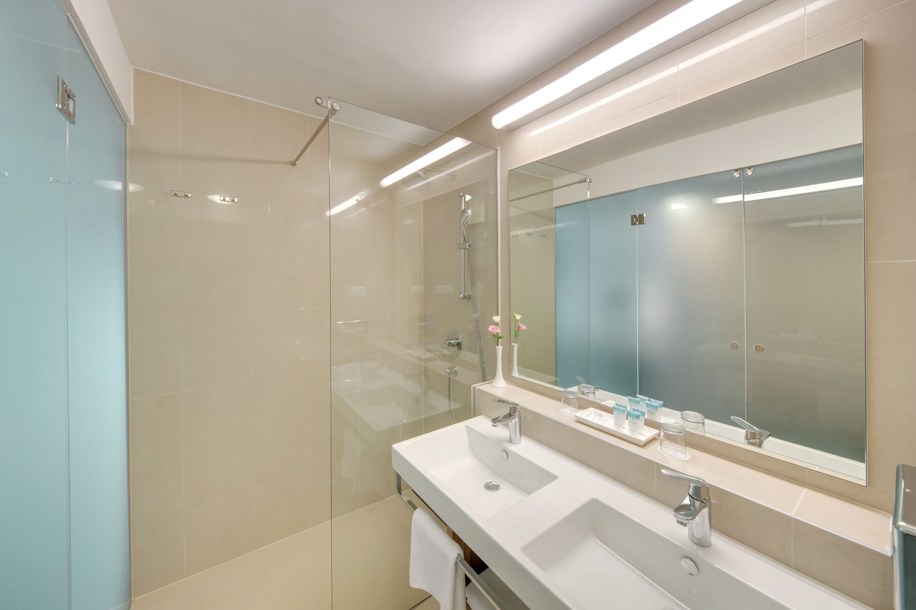 Ein modernes Badezimmer mit einer Duschkabine aus Glas, einem großen Spiegel und zwei Waschbecken.