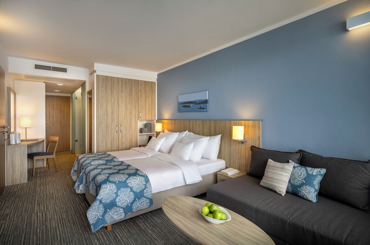 Une chambre d’h ôtel avec un lit, un canapé, un bureau et un panier de fruits.