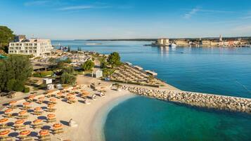 A coastal hotel with a beach, clear blue waters, and a marina.