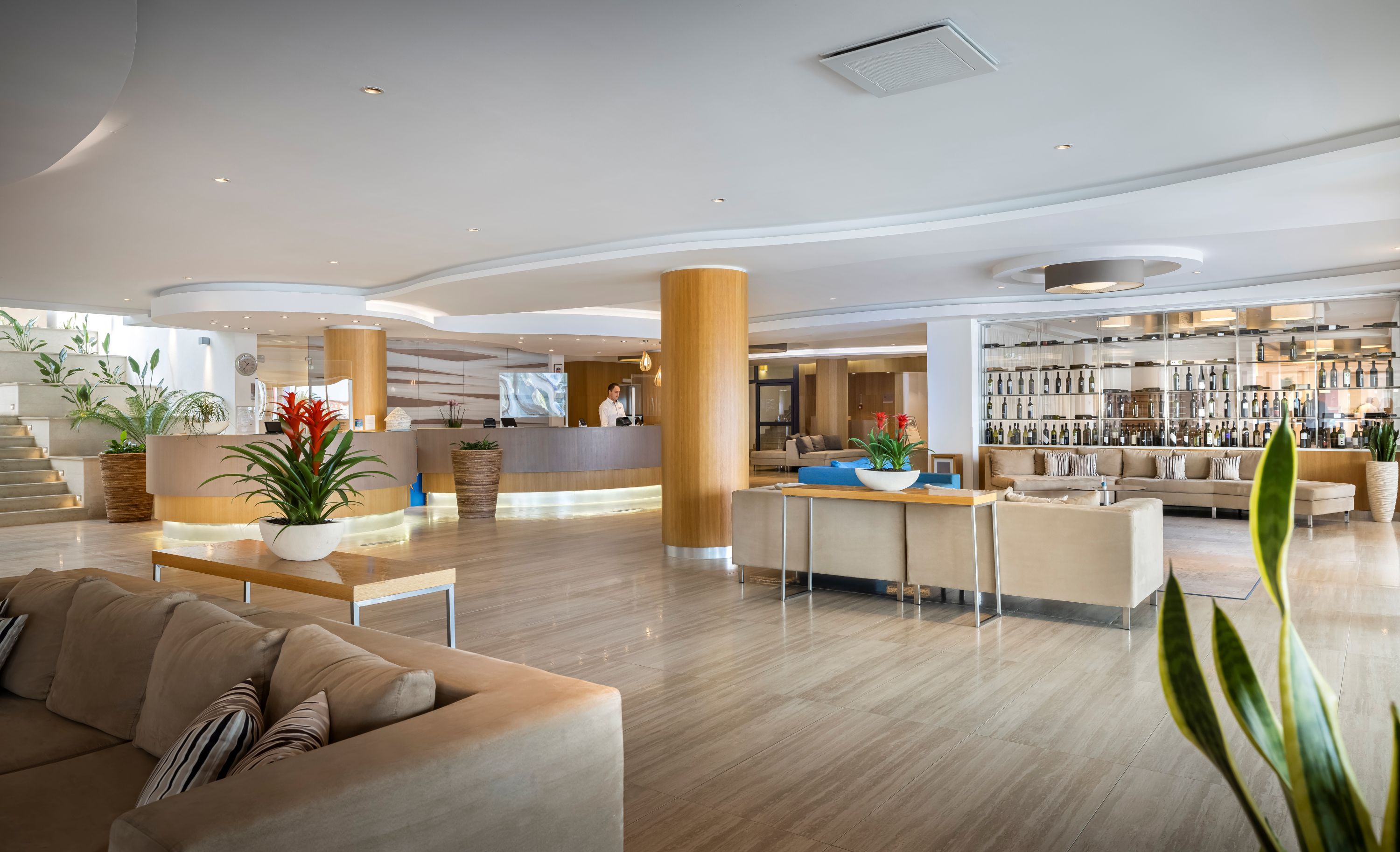 A modern hotel lobby with a reception desk, seating area, and a bar with a wine display.