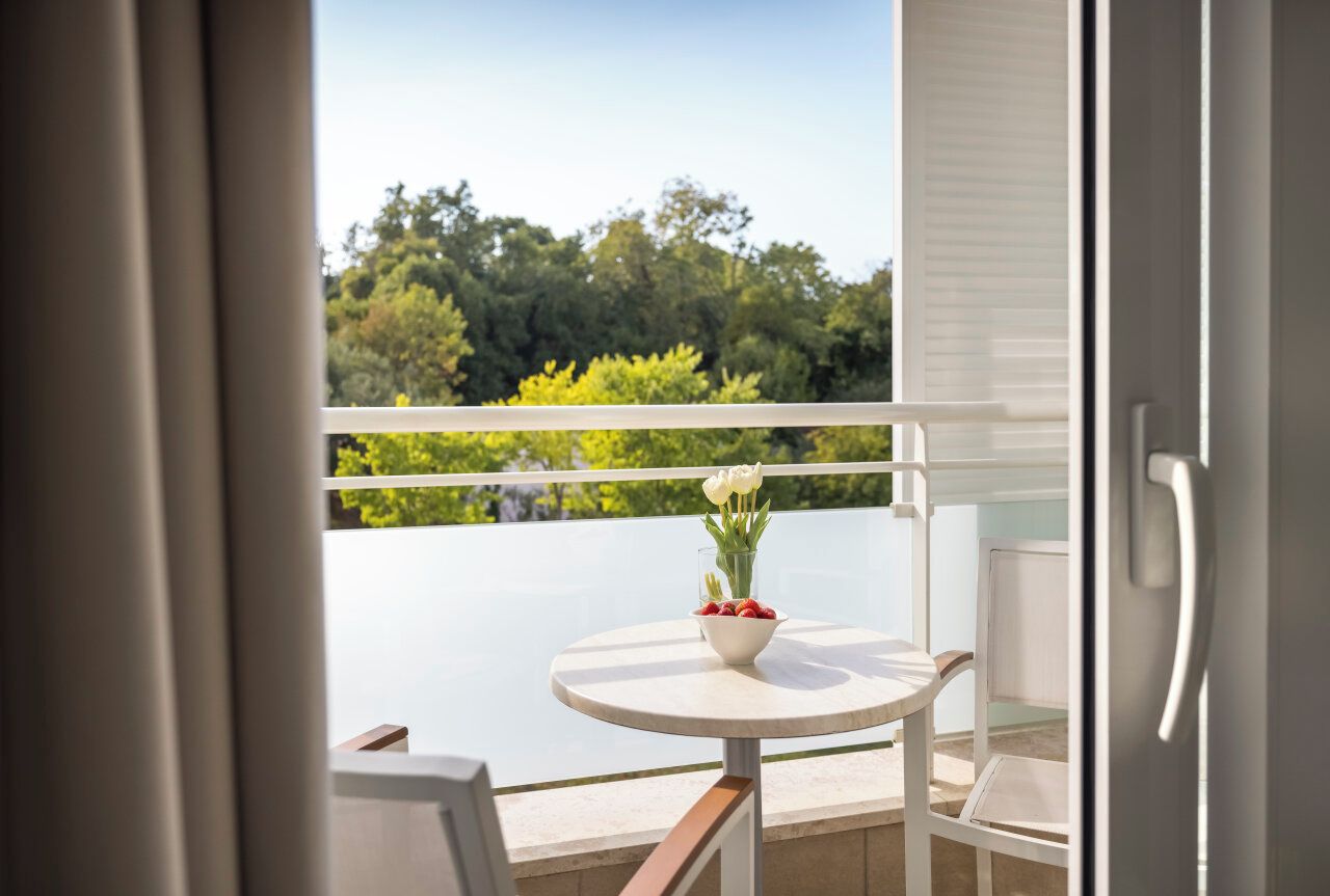 A balcony with a round table, a bowl of fruit, and a vase of flowers.