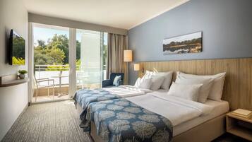 A hotel room with a balcony, a bed with a headboard, a TV mounted on the wall, and a painting above the bed.