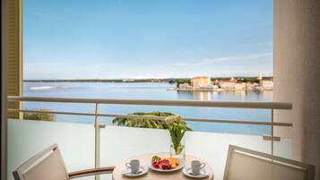 Ein Balkon mit Tisch für zwei Personen, einer Blumenvase und einer Platte mit Obst und Gebäck.