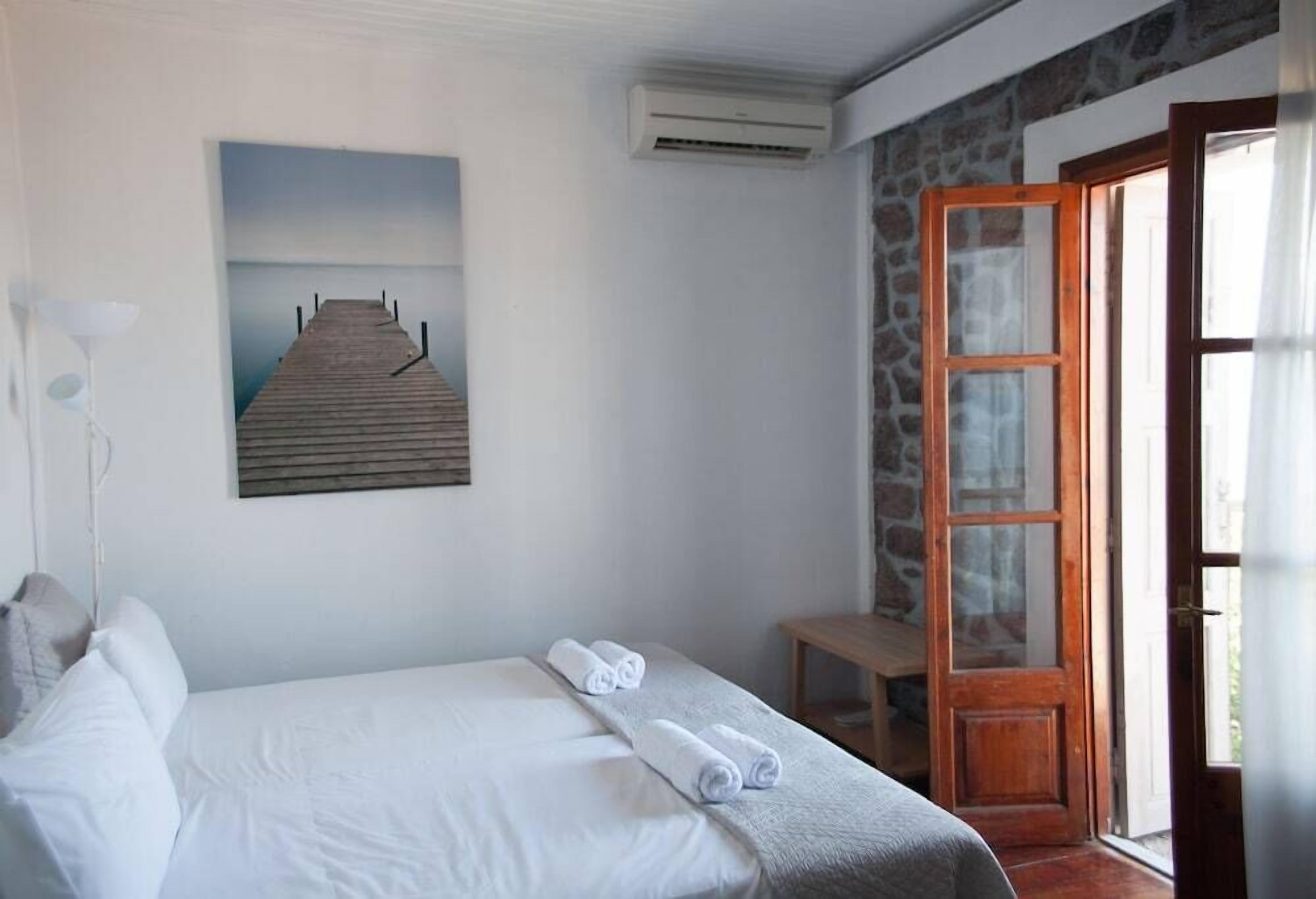 Quarto com cama, um quadro de um cais, aparelho de ar condicionado e porta de madeira.