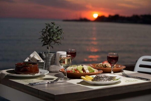 A table set for dinner with a sunset view, including a plant, wine glasses, and plates of food.