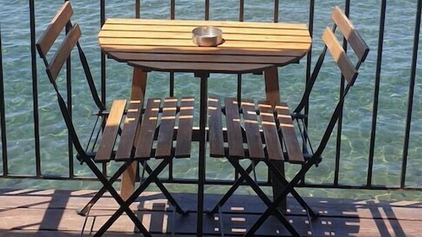 Eine Holzterrasse mit Tisch und Stühlen mit Blick auf ein Gewässer.