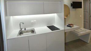 Eine moderne Küche mit Spüle, Mikrowelle und einer kleinen Arbeitsfläche. An der Wand ist ein Fernseher befestigt und eine Tür führt in einen anderen Raum.