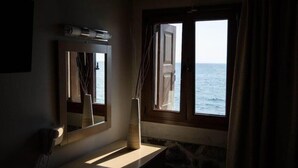 Ein Zimmer mit großem Fenster und Meerblick, einem Spiegel und einer Vase auf einer Ablagefläche.