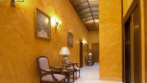 A hallway with wooden chairs, a lamp, and framed pictures on the wall.