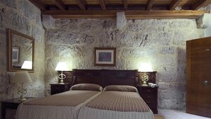 A bedroom with two beds, stone walls, wooden beams, a wooden door, and bedside lamps.