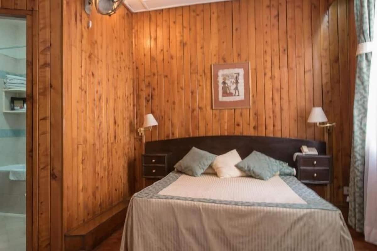 A wooden-paneled room with a bed, bedside tables, and a framed picture on the wall.