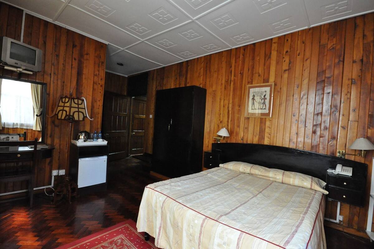 A room with a bed, a desk with a chair, a wardrobe, a television, and a window with curtains.