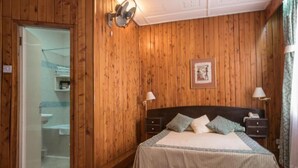 Una habitación con paneles de madera, una cama, lámparas de noche, un cuadro en la pared y una puerta que da al baño.