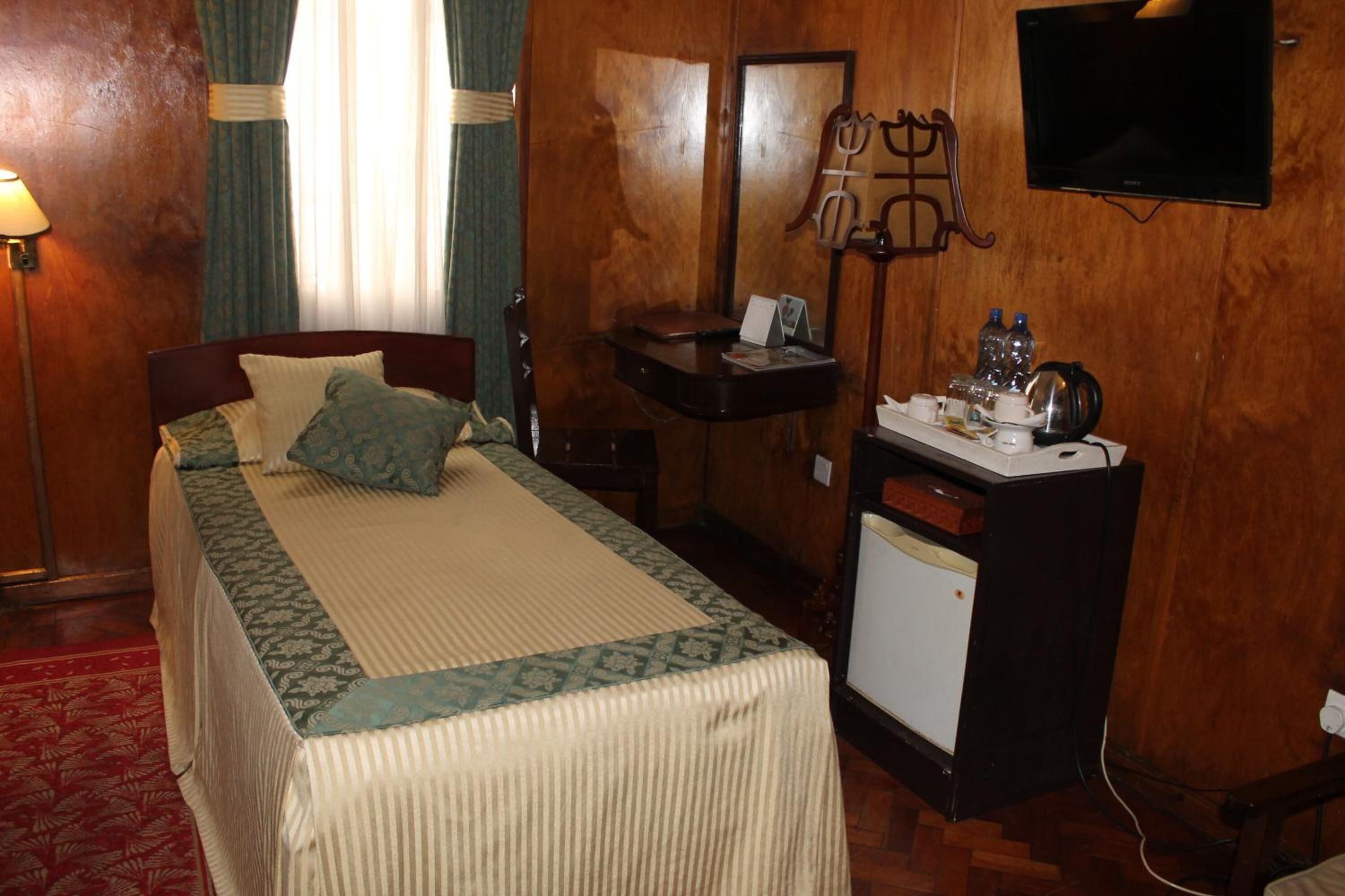 Ein Hotelzimmer mit Bett, Schreibtisch mit Computer, Wand-Fernseher und kleinem Kühlschrank.