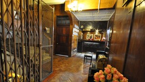 Un pasillo con suelo de madera, una reja de metal y un mostrador de recepción con un jarrón de flores.