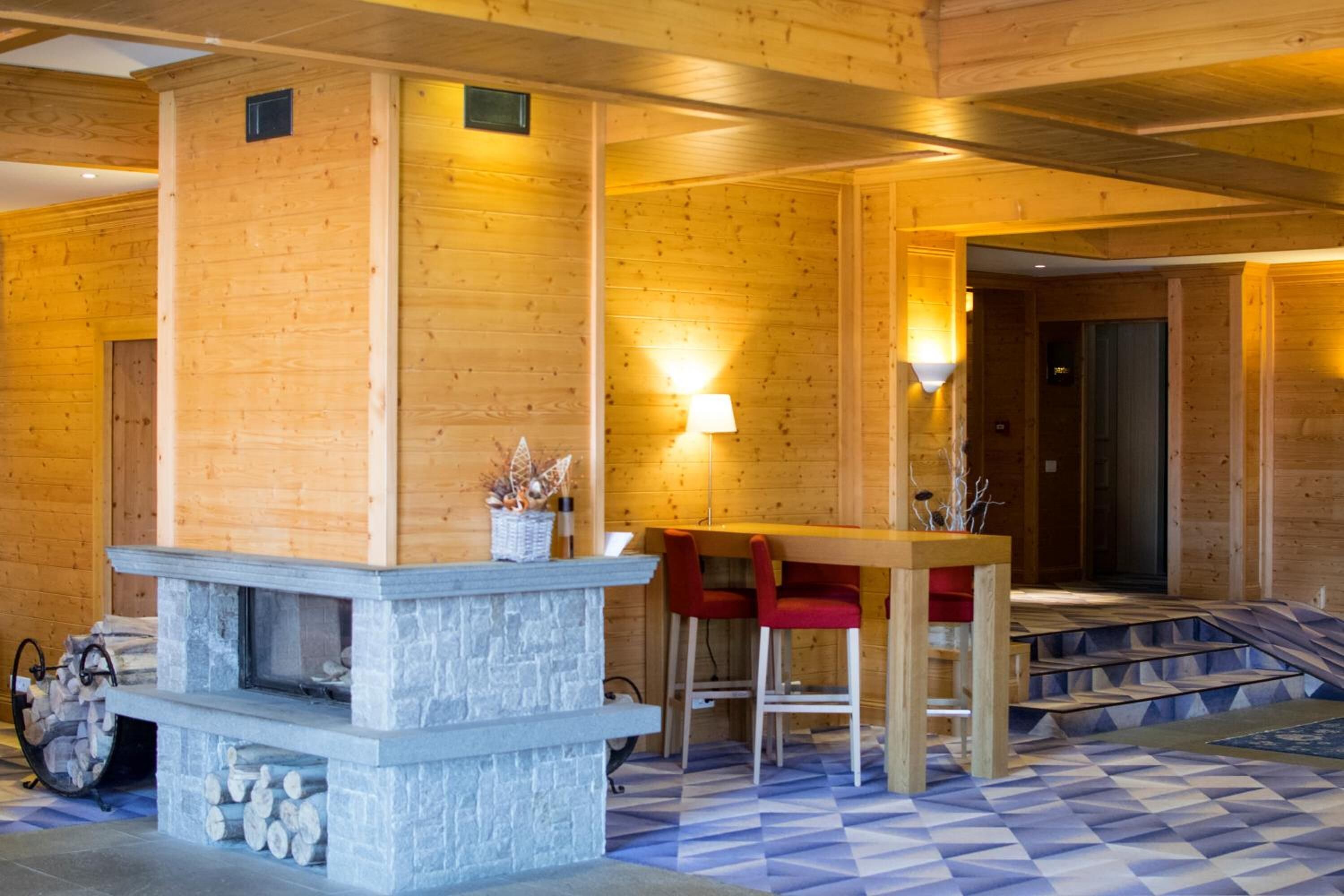 A wooden interior with a stone fireplace, a bar area with red chairs, and a checkered floor.