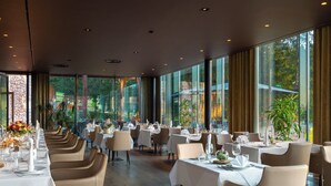 Un restaurante con mesas largas, sillas y amplios ventanales que ofrecen vistas al exterior.