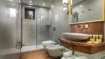 Uma casa de banho moderna com chuveiro em cabine de vidro, uma pia grande com bancada de mármore e um espelho com iluminação.