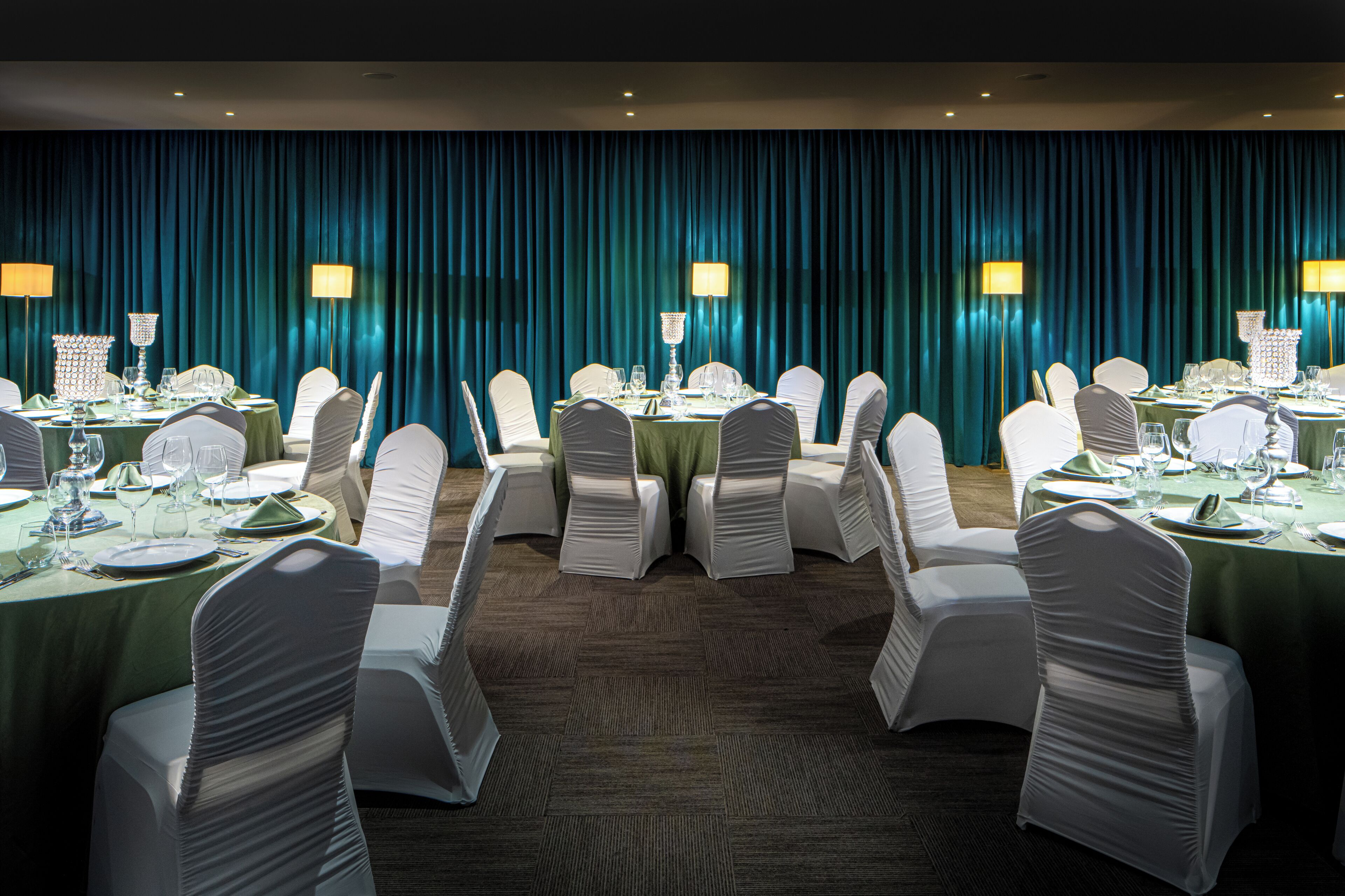 A banquet hall with round tables set for dining, white chairs, and teal curtains.