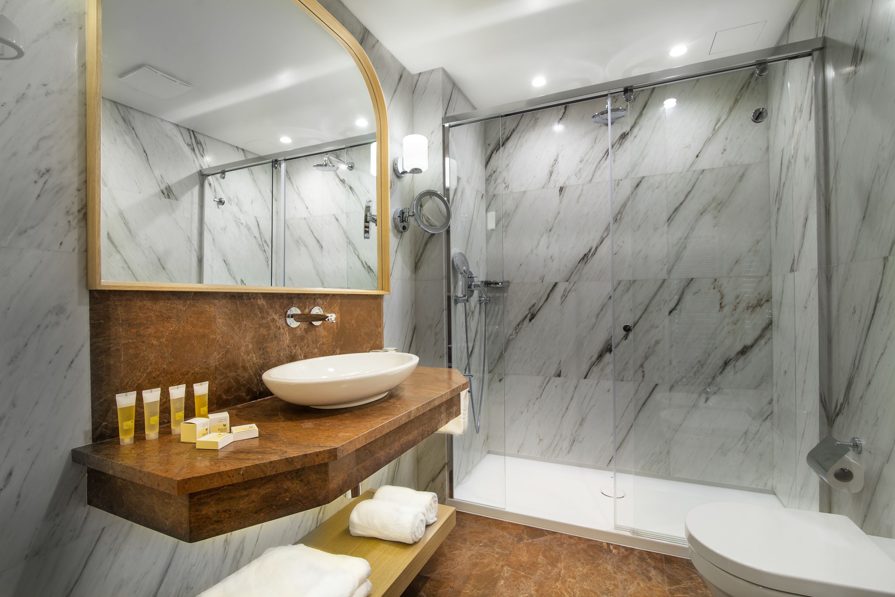 Un baño moderno con tocador de mármol, un espejo grande, ducha con cerramiento de vidrio y un área separada para el inodoro.