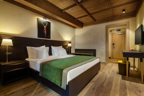 Ein Hotelzimmer mit einem großen Bett, einem Holzkopfstück, einer grünen Tagesdecke, einem Nachttisch mit einer Lampe und einem angebrachten Fernseher.