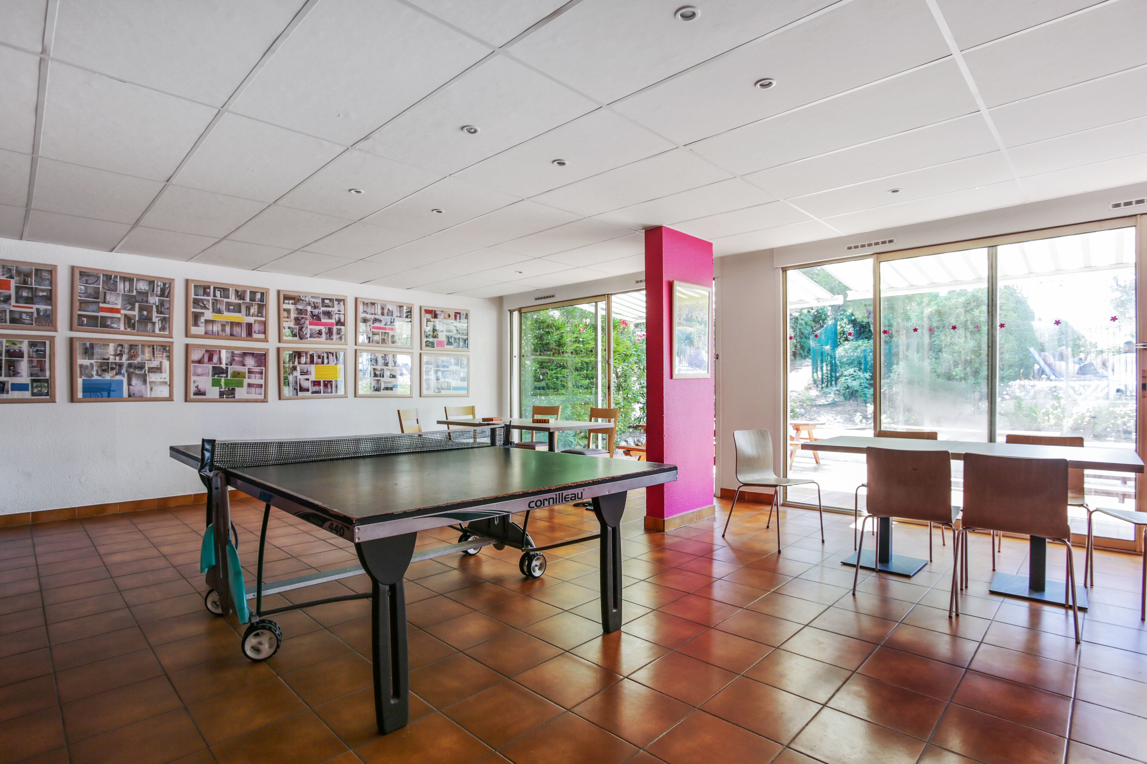 A spacious room with a ping pong table, chairs, and a wall displaying various framed pictures.