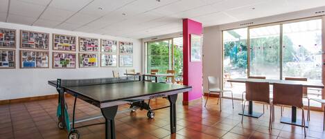 A spacious room with a ping pong table, chairs, and a wall displaying various framed pictures.